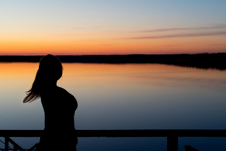 Young woman at sunset near lake silhouetteの写真素材
