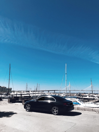 Luxury black car parked near yachts marine at sunny dayの写真素材