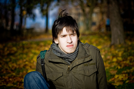 Young man sitting in autumn park at the groundの写真素材