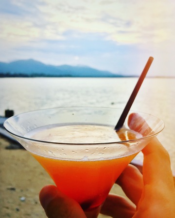 Man with glass of cocktail at the beach in the evening at vacationの写真素材