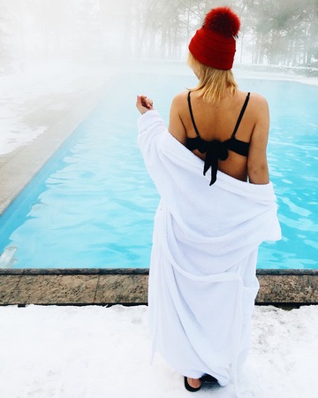 Young blonde woman in bathrobe and red hut near outdoor swimming pool at winter day.の写真素材
