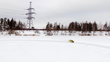 Car drives by icy track on snow covered lake at winter. Aerial view. Sport car racing on snow race track in winter. Driving a race car on a snowy roadの写真素材