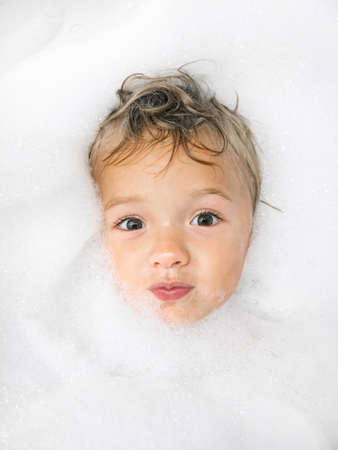 A portrait of a child who is immersed in a bath full of bubbles.の写真素材