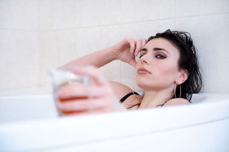 Beautiful young woman lies in the bathroom with a glass in her hand.の写真素材