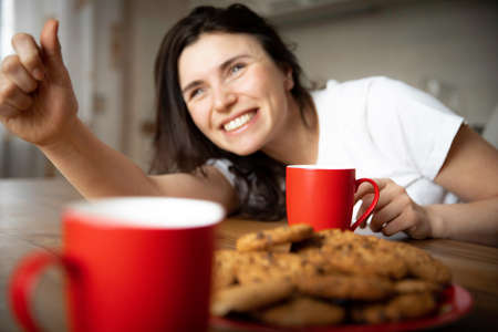Young woman drinks coffee with cookies at home kitchenの写真素材