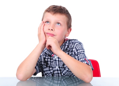 small boy sitting near table and thinkingの写真素材