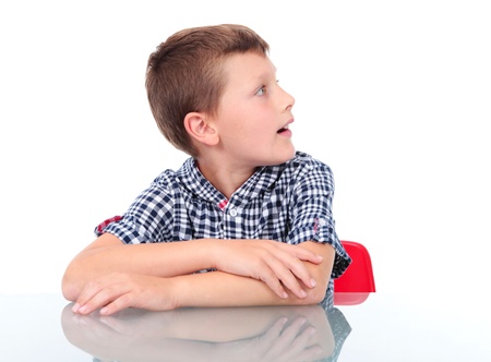 surprised boy sitting near table and looking at left の写真素材