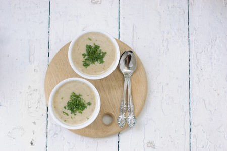 Mushroom soup with parsley in white ceramic bowl and spoon on a wooden board