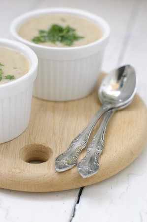 Mushroom soup with parsley in white ceramic bowl and spoon on a wooden boardの写真素材