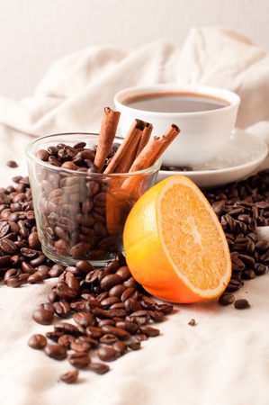 A cup of coffee, half an orange and coffee beans and cinnamon on linenの写真素材