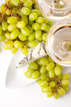 Two glasses of white wine, blue cheese and a bunch of white grapes on white backgroundの写真素材