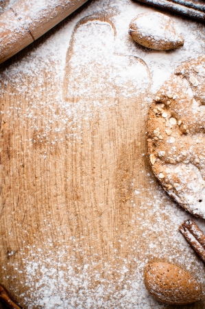Christmas and holiday baking background, flour, bakeware, heart, cinnamon, cookies and almonds on a wooden board, viewed from aboveの写真素材