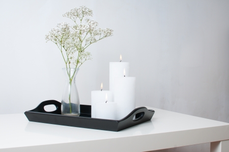 Branch in a vase, and four white candles burning on a black tray on a white table in an interiorの写真素材
