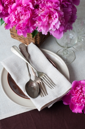 Beautiful table setting with pink peonies, vintage cutlery and brown tablecloth の写真素材