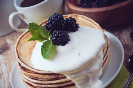 A stack of fresh, homemade pancakes with blackberries and whipped cream on a wooden table, a healthy breakfast, close-up.の写真素材