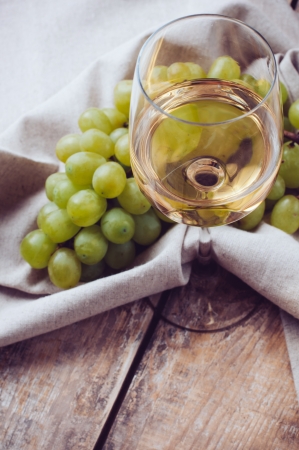 A glass of white wine, grapes, coarse linen cloth on a wooden board, closeupの写真素材