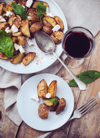 Homemade rustic dinner: a glass of wine and a baked potato with soft cheese and fresh basil in a...