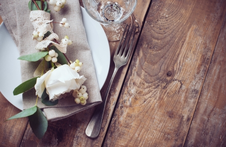Vintage table setting with floral decorations, napkins, white roses, leaves and berries on a wooden board backgroundの写真素材