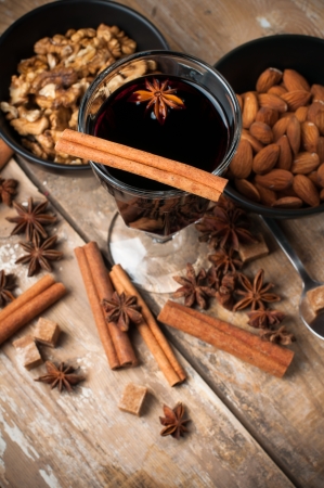A glass of hot mulled wine, spices, cinnamon, star anise, brown sugar and nuts on a wooden boardの写真素材