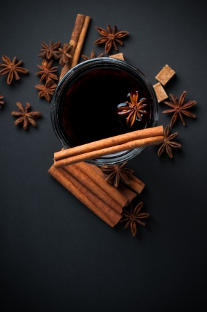 A glass of hot mulled wine, spices, cinnamon, star anise, brown sugar and nuts on a black background in studioの写真素材