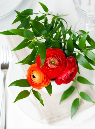 Bouquet of red buttercups with leaves in a white ceramic vase on a festive tableの写真素材