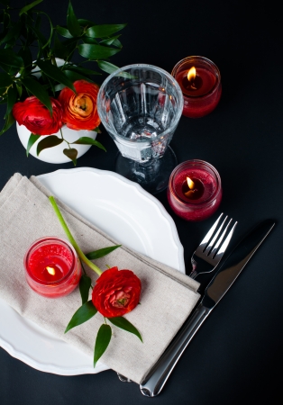 Festive dining table setting with red buttercup flowers, candles, napkins and shiny new cutlery on a black backgroundの写真素材
