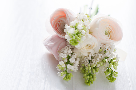 Beautiful delicate festive wedding bouquet of flowers, buttercups and white lilac on a white painted wooden board.の写真素材