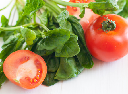 Vegetable background, tomatoes and spinach leaves on a white wooden board, food in kitchen.の写真素材