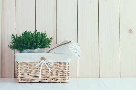 Home decor: vintage wicker basket, house plant and a stack of linen napkins on a wooden board  background, cozy composition retro style, soft pastel colors.の写真素材