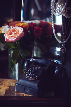 Old vintage black rotary phone and a bouquet of fresh roses on an old dresser in interior, retro style home decorの写真素材