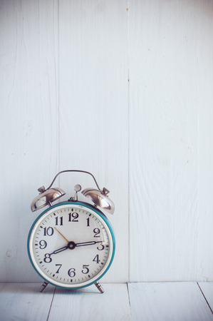 Big old vintage alarm clock with bells, painted white wooden backgroundの写真素材