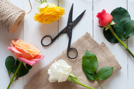 Floral arrangement, vintage floristic background, colorful roses, antique scissors and a rope on white painted wooden tableの写真素材
