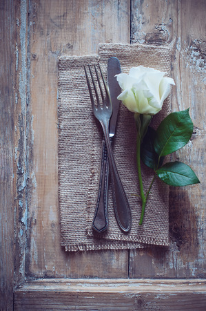 Vintage cutlery, antique silverware, fork, knife and a rose flower with rough cloth on an old wooden backgroundの写真素材
