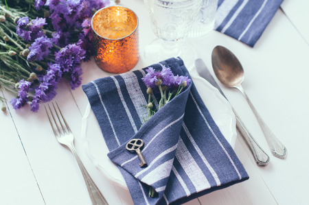 Vintage home table setting with blue napkins, antique cutlery, old key and purple cornflowers on...