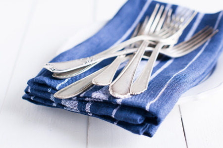 Delicate vintage silverware on blue linen napkin in a plate, antique cutlery om white wooden board backgroundの写真素材