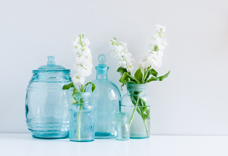 Vintage home decor background, white matthiola flowers in different blue glass bottles vases and antique jars on a shelf by the wallの写真素材