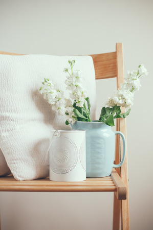 Vintage home decor, white matthiola flowers in a blue jug on a chair with pillows by the wallの写真素材