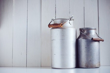 Two old vintage aluminum milk cans, painted white wooden board, rustic backgroundの写真素材