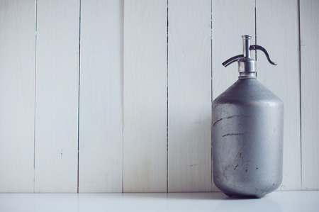 An old vintage aluminum siphon, antique seltzer soda bottle, painted white wooden board, rustic backgroundの写真素材