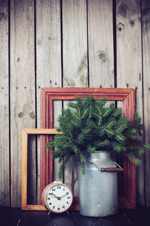 Rustic winter decorations, spruce branches in vintage can, vintage frames and alarm clock on a wooden boardの写真素材