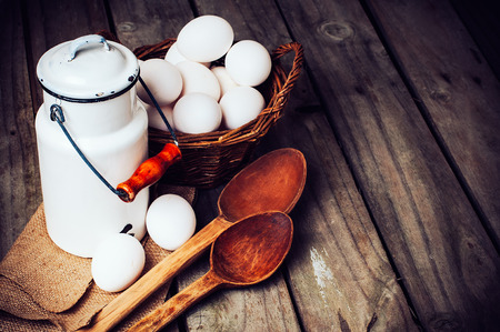Country kitchen Still Life, enamel milk can, eggs in a wicker basket and wooden spoons on a background of the old board, grunge styleの写真素材