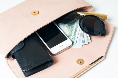 Cosmetics, sunglasses, money, purse and smartphone in an open beige woman's clutch handbag on a white background.の写真素材