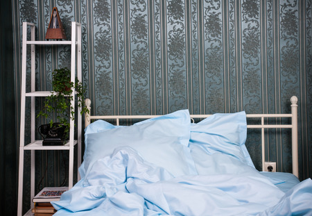 Cozy bedroom interior, double bed with light blue bed linen, pillows and shelves with vintage decorの写真素材