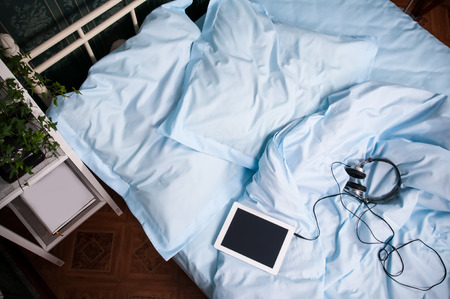 Cozy bedroom interior, double bed with light blue bed linen, pillows, tablet with headphones and shelves with vintage decor, shot from aboveの写真素材