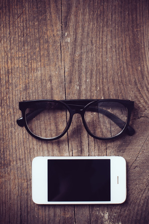 Smartphone and reading glasses on an old wooden board, hipster styleの写真素材