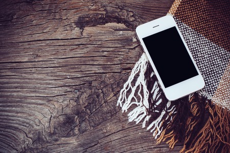 White smartphone, and brown plaid on an old wooden boardの写真素材
