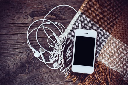 White smart phone with headphones and brown plaid on an old wooden boardの写真素材
