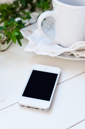 White smartphone, plants and ceramic cup on a white wooden tableの写真素材