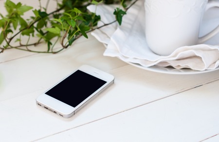 White smartphone, plants and ceramic cup on a white wooden tableの写真素材