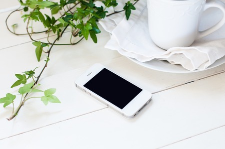 White smartphone, plants and ceramic cup on a white wooden tableの写真素材